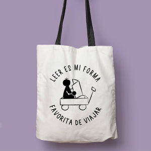 Tote bag natural con asa negra con la ilustración del personaje Lectorix y el texto "Leer es mi forma favorita de viajar"